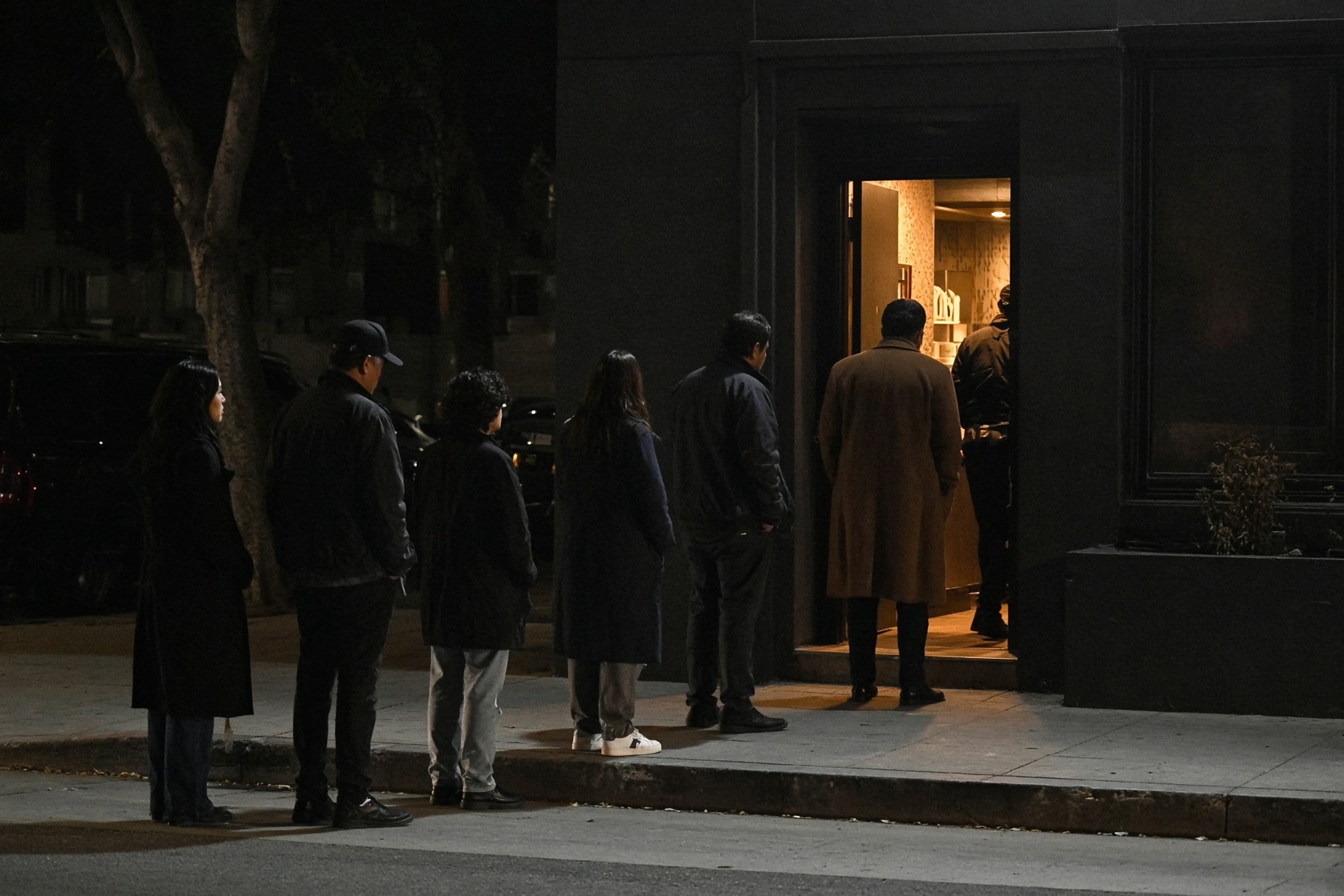 People waiting outside a dark doorway with warm light inside